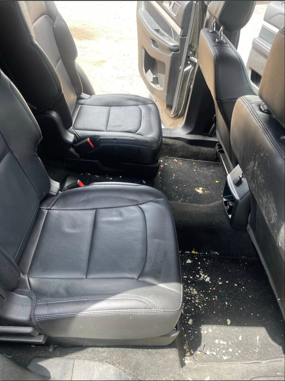 Second-row floor of a Chevrolet Tahoe before a ShineCraft interior detail — crumbs and debris scattered on the floor mats.